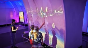 Adler Planetarium interactive spacewalk display in the Clark Family Welcome Gallery shows three young visitors gesturing toward a projected astronaut and the International Space Station. The immersive installation combines motion-sensing interaction, layered video projections, fabric surfaces, and blue-purple lighting inside the Museum Campus space museum in Chicago, Illinois – © 2026 David Oppenheimer – Performance Impressions photography archives https://performanceimpressions.com Adler Planetarium, Adler Planetarium Chicago, Adler Planetarium exhibit, Adler Planetarium interior, Clark Family Welcome Gallery, Welcome Gallery, Exploring Space, interactive spacewalk, spacewalk exhibit, astronaut exhibit, astronaut projection, interactive exhibit, interactive display, interactive projection, immersive exhibit, immersive display, immersive installation, motion sensing, motion sensor, gesture control, gesture controlled, visitor interaction, projection wall, video projection, projected image, space projection, spacewalk, astronaut, space station, International Space Station, ISS, space exploration, human spaceflight, outer space, space, stars, astronomy, astrophysics, planetarium, space museum, astronomy museum, science museum, museum, museum interior, museum exhibit, science exhibit, astronomy exhibit, space exhibit, educational exhibit, interactive museum, science education, space education, astronomy education, STEM, STEAM, children, girls, young visitors, museum visitors, visitors, interaction, hands, gestures, shadows, experiential learning, hands on learning, hands on exhibit, digital exhibit, digital media, interactive media, multimedia, multimedia exhibit, projection mapping, immersive media, exhibition design, exhibit design, interactive design, museum design, visual technology, display technology, motion detection, space simulation, astronaut spacewalk, astronaut floating, astronaut in space, space station platform, orbital station, orbit, microgravity, space science, space technology, cosmic imagery, star field, blue lighting, purple lighting, LED lighting, colored lighting, dramatic lighting, illuminated exhibit, fabric walls, fabric panels, sheer fabric, projection fabric, aluminum tubing, futuristic interior, futuristic design, futuristic architecture, Thomas Roszak Architecture, Thomas Roszak Architects, Snibbe Interactive, Second Story, Graham Plumb, Clark Family, Grainger Sky Theater, Museum Campus, Chicago Museum Campus, Northerly Island, Chicago lakefront, 1300 South DuSable Lake Shore Drive, 1300 S DuSable Lake Shore Dr, 1300 South Lake Shore Drive, 1300 S Lake Shore Drive, Chicago, Chicago Illinois, Chicago IL, Illinois, 60605, Chicago attraction, Chicago museum, Chicago science museum, Chicago planetarium, family attraction, educational attraction, cultural institution, nonprofit, 501c3, Museums in the Park, Chicago Park District, United States, licensing, image licensing, commercial imagery, photography licensing, art, print, fine art, commercial photography, David Oppenheimer, horizontal, 1-15213827141
