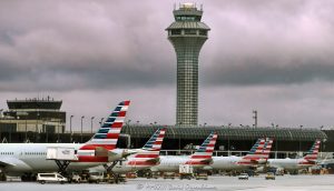 Chicago O’Hare International Airport Terminal 3 with American Airlines jets parked at the K gates beneath dark clouds, with the jet bridges, the airport apron, and an air traffic control tower in the background. The terminal section at the left edge houses the American Airlines flagship lounge, the Admirals Club – © 2026 David Oppenheimer – Performance Impressions photography archives https://performanceimpressions.com Chicago O’Hare International Airport, Chicago O’Hare Airport, O’Hare International Airport, O’Hare Airport, Chicago O’Hare, Chicago airport, ORD, O’Hare Terminal 3, Chicago O’Hare Terminal 3, Terminal 3, Terminal 3 Chicago, American Airlines jets, American Airlines O’Hare, American Airlines ORD, American Airlines Terminal 3, O’Hare K gates, Terminal 3 K gates, K gates, Concourse K, K Concourse, 10000 W O’Hare Avenue, 10000 West O’Hare Avenue, O’Hare, O’Hare Chicago, O’Hare community area, Northwest Side Chicago, Chicago Illinois, Chicago IL, 60666, Orchard Field, former Orchard Field, airport, terminal, airport terminal, gates, airport gates, boarding gates, gate area, aviation, commercial aviation, air travel, airline, airlines, jet, jets, aircraft, airplanes, airliners, passenger jets, passenger aircraft, commercial aircraft, parked jets, parked aircraft, aircraft parking, American Airlines, American, American Airlines Group, AAdvantage, Oneworld, American Airlines hub, airline hub, hub airport, American Airlines fleet, American Airlines livery, aircraft tails, jet bridge, jet bridges, apron, airport apron, ramp, airport ramp, tarmac, ground operations, airline operations, airport operations, airfield, terminal building, terminal exterior, airport exterior, building exterior, facade, air traffic control, air traffic control tower, airport control tower, control tower, ATC, ATC tower, O’Hare control tower, FAA, Federal Aviation Administration, Chicago Department of Aviation, CDA, American Airlines Flagship Lounge, American Flagship Lounge, Flagship Lounge, Flagship Lounge ORD, American Airlines Admirals Club, Admirals Club, Admirals Club ORD, Admirals Club lounge, American Airlines lounge, Terminal 3 lounge, H K connector, dark clouds, cloudy sky, overcast sky, cloud cover, weather, airport weather, aviation weather, dramatic sky, airport architecture, terminal architecture, transportation architecture, airport photography, aviation photography, transportation, travel, business travel, Chicago aviation, Illinois aviation, United States, licensing, image licensing, commercial imagery, photography licensing, art, print, fine art, commercial photography, David Oppenheimer, horizontal, 1-15213827141