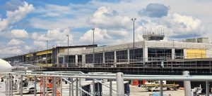 Asheville Regional Airport AVL Forward terminal construction in Fletcher near Asheville, North Carolina, viewed from the airport apron with scaffolding and exposed structural steel framing revealing the open terminal structure during construction. The airport terminal modernization and expansion was designed by Gresham Smith and is being built by Hensel Phelps for the Greater Asheville Regional Airport Authority – © 2026 David Oppenheimer – Performance Impressions photography archives https://performanceimpressions.com Asheville Regional Airport, Asheville Airport, Asheville Regional, Asheville airport terminal, Asheville terminal, Asheville airport construction, Asheville construction, Asheville airport expansion, AVL Forward, AVL Forward terminal, AVL Forward project, AVL terminal, AVL terminal construction, AVL construction, AVL airport, AVL, KAVL, airport terminal, terminal, terminal construction, airport construction, terminal expansion, airport expansion, terminal modernization, airport modernization, terminal renovation, new terminal, new airport terminal, airport building, terminal building, building construction, construction, construction site, construction project, construction progress, under construction, building under construction, unfinished building, unfinished structure, work in progress, scaffolding, scaffold, scaffolds, structural steel, steel structure, steel frame, steel framing, exposed steel, exposed structure, exposed framing, girders, girder, steel girders, beams, beam, steel beams, columns, steel columns, structural frame, building frame, open structure, open framing, building structure, structural construction, steel construction, construction detail, construction architecture, architecture, airport architecture, terminal architecture, aviation architecture, architectural construction, architectural engineering, engineering, structural engineering, civil engineering, infrastructure, airport infrastructure, aviation infrastructure, transportation infrastructure, infrastructure construction, commercial construction, large scale construction, capital project, airport development, airport improvement, terminal development, aviation construction, airside construction, airport operations, construction operations, airport apron, apron, aircraft apron, airport ramp, ramp, tarmac, airfield, airside, airport ground, ground boarding, passenger operations, aviation, airport, regional airport, commercial airport, transportation, air travel, Gresham Smith, Gresham Smith Asheville, Gresham Smith aviation, architect, architects, airport architect, terminal architect, aviation architect, architecture firm, Brad Sucher, structural engineer, civil engineer, engineering firm, interior design, airport planning, terminal planning, experiential design, wayfinding, Hensel Phelps, Hensel Phelps Construction, Hensel Phelps Asheville, construction manager, construction management, CM at Risk, contractor, general contractor, airport contractor, aviation contractor, Greater Asheville Regional Airport Authority, Asheville Regional Airport Authority, GARAA, airport authority, Asheville, Asheville North Carolina, North Carolina, NC, Western North Carolina, WNC, Fletcher, Fletcher North Carolina, Henderson County, Buncombe County, Blue Ridge, Blue Ridge Mountains, 61 Terminal Drive, Terminal Drive, Airport Road, 28732, United States, USA, airport photography, construction photography, architecture photography, architectural photography, infrastructure photography, aviation photography, transportation photography, industrial photography, documentary photography, editorial photography, commercial photography, Asheville photography, North Carolina photography, construction art, architecture art, airport art, Asheville art, photographic print, fine art print, archival print, gallery print, collector print, wall art, licensing, image licensing, commercial imagery, photography licensing, art, print, fine art, commercial photography, clouds, sunny, blue sky, summer, David Oppenheimer, Performance Impressions, Performance Impressions photography archives, horizontal, 1-15156784411