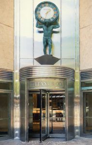 Tiffany & Co. Atlas Clock on Chicago’s Magnificent Mile Tiffany & Co. Atlas Clock above the entrance at 730 North Michigan Avenue in Chicago anchors a tightly framed view of the Magnificent Mile storefront, with the Atlas figure holding a Roman-numeral clock above the revolving doors. Tiffany & Co. signage, warm metallic tones, curved entrance details, and strong vertical facade lines give the photograph a surreal, highly rendered fine-art character in Chicago, Illinois – © 2026 David Oppenheimer – Performance Impressions photography archives https://performanceimpressions.com