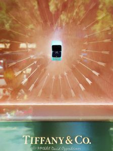 Tiffany & Co. Diamond Ring Display in a Heart of Light Tiffany & Co. window display at 730 North Michigan Avenue in Chicago centers on a depiction of a diamond ring in an open black velvet-lined Tiffany Blue box, appearing to float within a heart formed by glowing arrows in orange, red, and yellow light. Reflections in the glass and Tiffany & Co. signage beneath the display create a surreal fine-art composition along the Magnificent Mile in Chicago, Illinois – © 2026 David Oppenheimer – Performance Impressions photography archives https://performanceimpressions.com Tiffany & Co., Tiffany and Co, Tiffany & Co. Chicago, Tiffany Chicago, Tiffany Chicago store, Tiffany Michigan Avenue, Tiffany jewelry store, Tiffany storefront, Tiffany window display, Tiffany diamond ring, Tiffany engagement ring, Tiffany Blue, Tiffany blue box, Tiffany ring box, Tiffany signage, diamond ring, engagement ring, diamond jewelry, fine jewelry, luxury jewelry, jewelry box, ring box, open ring box, black velvet, velvet lining, heart of light, arrow heart, heart shape, heart display, illuminated arrows, glowing arrows, floating ring box, hovering box, surreal display, abstract display, window display, store window, retail window, storefront display, jewelry display, luxury display, visual merchandising, window dressing, retail design, display design, product display, luxury retail, luxury boutique, jewelry store, storefront, glass window, brand signage, luxury branding, reflections, window reflections, glass reflections, layered reflections, urban reflections, abstract reflections, reflection photography, illuminated display, glowing window, warm light, fiery light, orange, red, yellow, pastel colors, saturated color, vivid color, colorful, surreal, surrealism, surreal photography, surreal art, dreamlike, abstract, abstraction, abstract photography, abstract art, conceptual photography, conceptual art, fine art photography, fine art photograph, art photography, contemporary photography, creative photography, urban fine art, photorealism, photo realism, photorealistic, painterly, painterly photography, visual illusion, optical illusion, luxury still life, still life photography, retail photography, storefront photography, window display photography, commercial art, luxury art, jewelry art, diamond art, diamond ring art, Tiffany art, Tiffany window art, Tiffany photography, Tiffany print, Tiffany poster, Tiffany wall art, Chicago art, Chicago photography, Chicago wall art, Michigan Avenue art, Magnificent Mile art, surreal wall art, abstract wall art, luxury wall art, fine art print, photographic print, archival print, gallery print, collector print, collectible art, art poster, fine art poster, wall art, wall decor, luxury decor, home decor, office decor, interior design, statement art, art collector, photography collector, Tiffany collector, love, romance, engagement, proposal, iconic blue box, blue box, 730 North Michigan Avenue, 730 N Michigan Avenue, North Michigan Avenue, Michigan Avenue, Magnificent Mile, Mag Mile, Near North Side, downtown Chicago, Chicago shopping, Magnificent Mile shopping, Chicago, Chicago Illinois, Chicago IL, Illinois, 60611, LVMH, LVMH Group, LVMH Tiffany, Tiffany LVMH, Tiffany parent company, LVMH Moët Hennessy Louis Vuitton, LVMH Moet Hennessy Louis Vuitton, LVMH luxury group, luxury conglomerate, luxury goods, watches and jewelry, LVMH stock, LVMH MC, LVMH ticker MC, Euronext Paris MC, LVMUY, LVMUY stock, OTC LVMUY, United States, licensing, image licensing, commercial imagery, photography licensing, art, print, fine art, commercial photography, Performance Impressions, David Oppenheimer, vertical, 1-15213827141