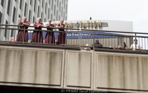 Women in Burgundy Dresses at Chicago Union Station Women in matching burgundy dresses and white bonnet-style head coverings stand near Chicago Union Station by South Riverside Plaza, waving toward a boat tour on the Chicago River. The scene frames a candid downtown Chicago moment with bridge railings, riverfront architecture, and the Adams Street entrance area of the historic rail terminal – © 2026 David Oppenheimer – Performance Impressions photography archives https://performanceimpressions.com Chicago Union Station, Union Station, Union Station Chicago, women in burgundy dresses, burgundy dresses, white bonnets, bonnet headwear, white head coverings, coordinated outfits, matching dresses, costume-like clothing, theatrical style, Handmaid’s Tale style, dystopian style, public moment, urban event, unusual sighting, boat tour, Chicago boat tour, river tour, tour boat, Chicago River, river, riverfront, waterfront, water, bridge railing, metal railing, weathered railing, South Riverside Plaza, Riverside Plaza, Adams Street entrance, Union Station Adams Street, Welcome to Chicago, West Loop, Near West Side, downtown Chicago, Chicago Illinois, Chicago IL, 60606, rail station, train station, railroad station, transportation, transit, Amtrak, Metra, architecture, architectural facade, facade, building exterior, exterior, Beaux Arts, Beaux-Arts architecture, Classical Revival, historic building, landmark building, Chicago Landmark, Graham Anderson Probst White, Graham Anderson Probst & White, Daniel Burnham, Chicago architecture, historic architecture, urban photography, street photography, documentary photography, people, women, group, waving, posing, summer daylight, city tour, tourism, travel, United States, licensing, image licensing, commercial imagery, photography licensing, art, print, fine art, commercial photography, David Oppenheimer, horizontal, 1-15156784411